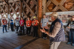 A person leads a presentation on a covered bridge along the trail.