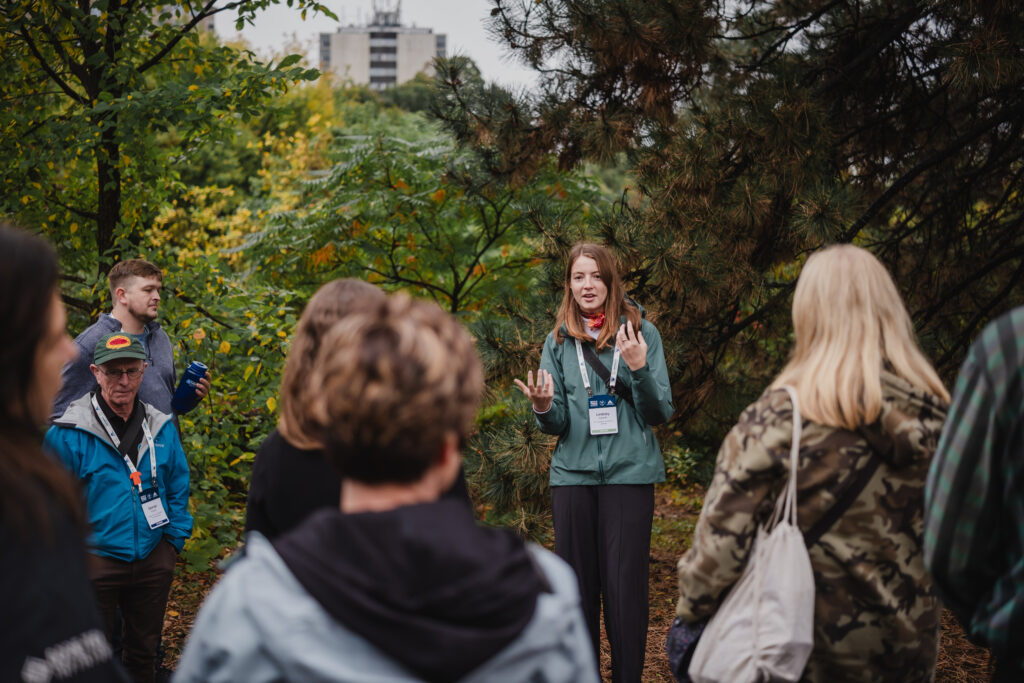 A person delivers a presentation surrounded by lush trees on the trail.